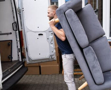 Möbellift Sinsheim Möbellift Sinsheim: Helfer tragen ein graues Sofa aus einem Transporter